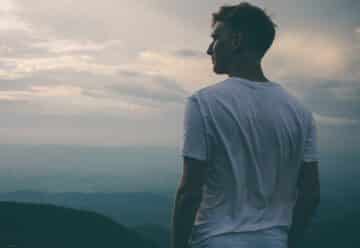 man standing facing mountains during sunset