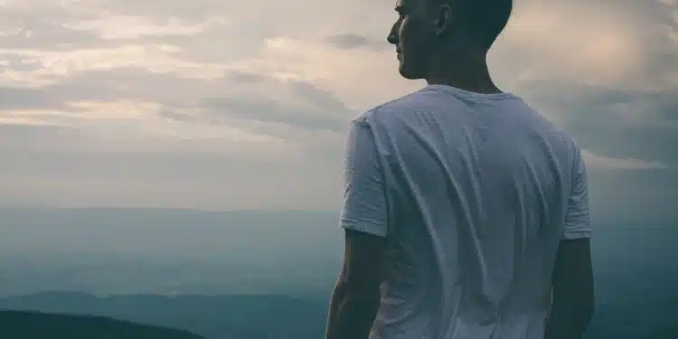 man standing facing mountains during sunset