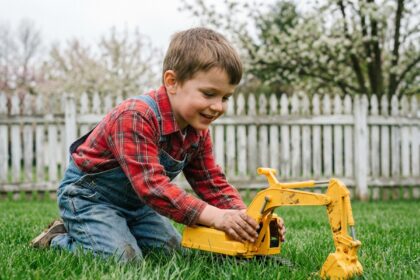 Jeune garçon en salopette pousse une pelle jaune dans le jardin